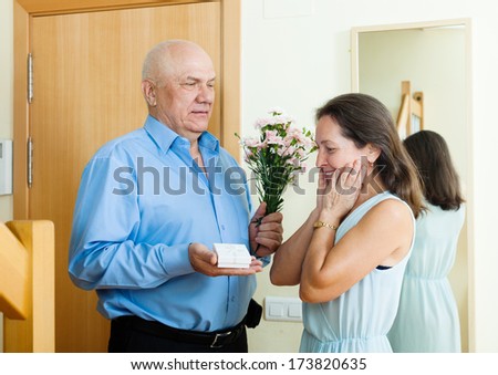 senior man came to  woman with present and flowers at home