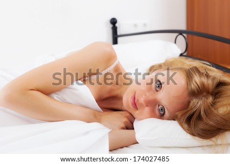 Blonde long-haired woman awaking up on white sheet in bed at home
