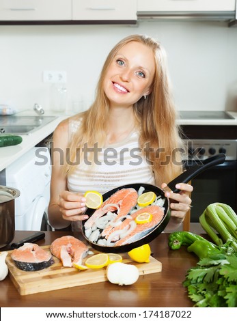 Smiling woman putting pieces lemon in fish at home kitchen