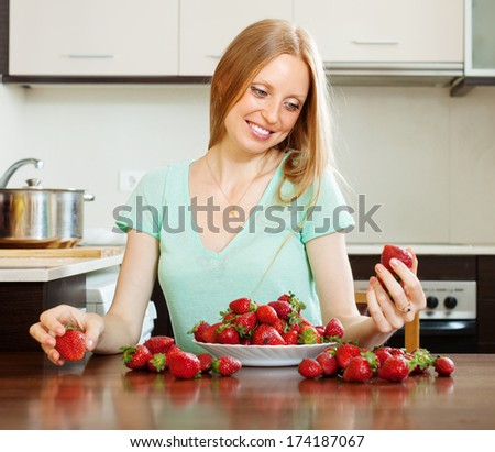 Happy blonde long-haired girl with strawberry in  kitchen