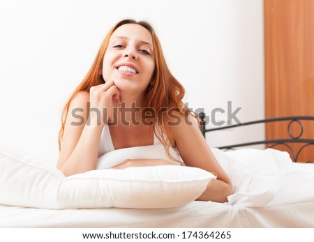 Long-haired young female wakes up in her bed at home
