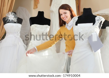 Smiling pretty bride chooses wedding gown at bridal boutique