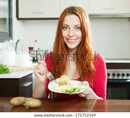 Casual positive girl in red eating jacket potatoes at home interior