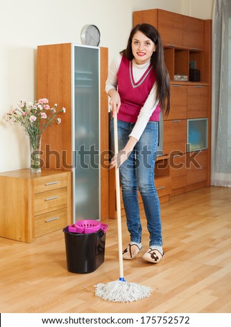 ordinary brunette woman washing parquet floor with mop in home