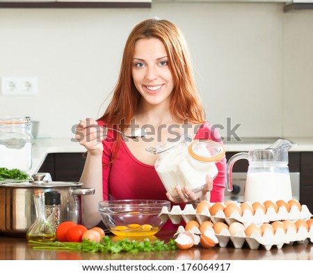 Smiling girl in red cooking omelet with flour in  kitchen