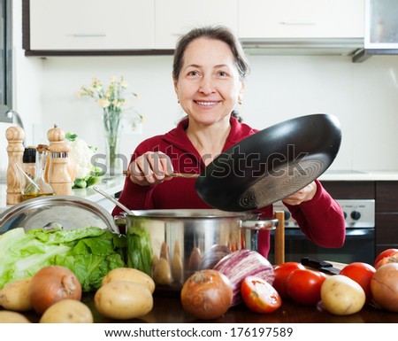 Happy mature woman cooking  with skillet in  kitchen