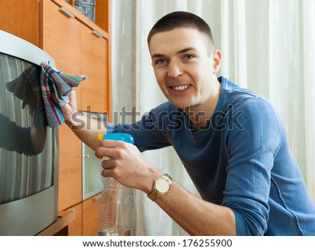 Smiling guy cleaning TV at living room