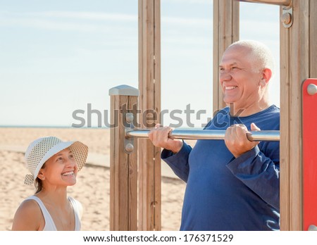 Mature couple together training on pull-up bar in summer