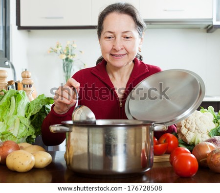 Smiling mature woman cooking soup with ladle in home kitchen