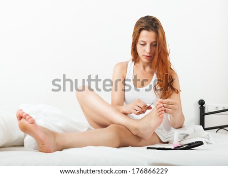 Beautiful red-haired girl cares for toenails with nail lacquer on a bad