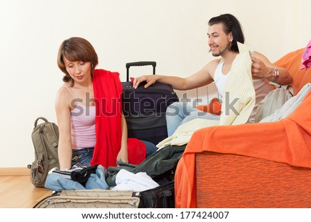 Smiling couple sitting on the orange couch and packs a suitcase at home