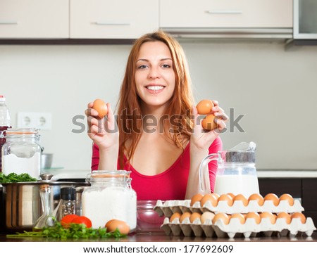 Smiling girl in red cooking omelet with eggs in home kitchen