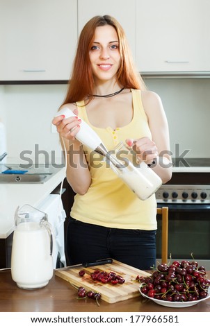 long-haired girl in yellow cooking milk shake with cherry at home kitchen