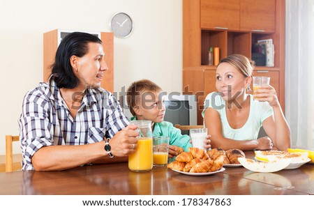 Happy adult couple with teenager having breakfast with juice in morning at home interior
