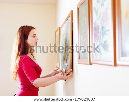 Long-haired girl hanging pictures in frames on wall