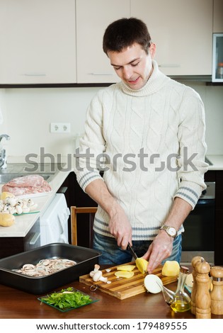 Handsome man cooking meat with  mushrooms and potatoes - cutting potatoes