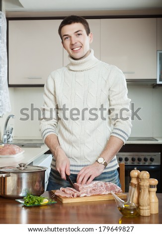 Handsome man cooking french-style meat at kitchen. Hands cutting meat