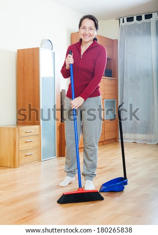 Smiling mature woman sweeping the floor in living room at home