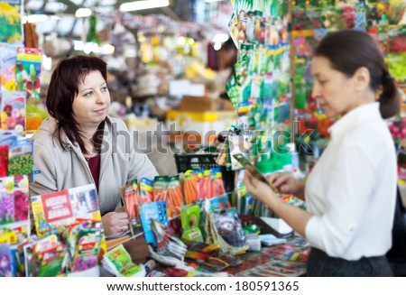woman selling seeds to mature buyer in store for gardeners. Focus on seller
