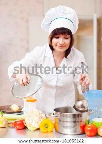 cook woman in toque cooks with vegetables in kitchen