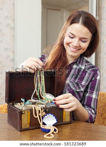 portrait of happy girl chooses jewelry in treasure chest at home