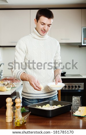 Handsome man cooking french-style meat. Adding grated cheese in roasting pan