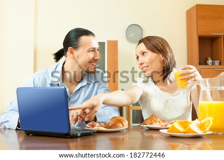 Happy ordinary couple looking e-mail in laptop during breakfast time at home
