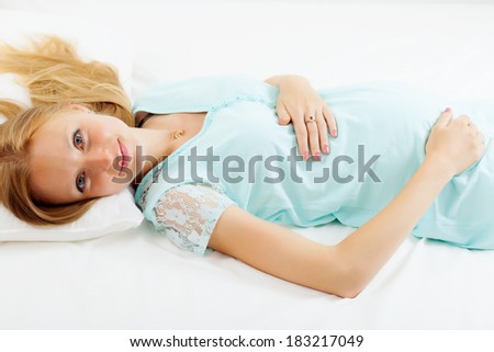 long-haired pregnancy woman in nightdress lying on bed in bedroom