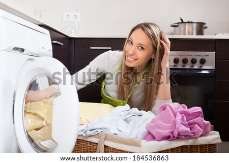 Home laundry. Happy blonde woman putting clothes in to washing machine  at home