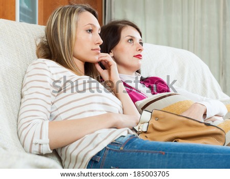 Two sadness girlfriends together on sofa in home
