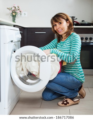Ordinary housewife in green using washing machine at home