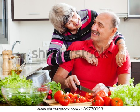 happy elderly couple cooking with vegetables and greens in home kitchen