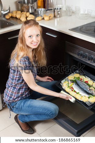 Smiling woman cooking raw fish in oven at home kitchen