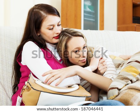 Young woman comforting crying friend at sofa in home