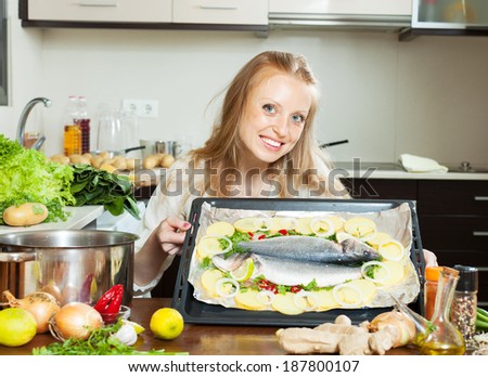 Cheeful housewife cooking fish and potatoes in sheet pan at home