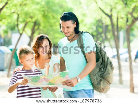 Happy family of three searching way at paper map in park