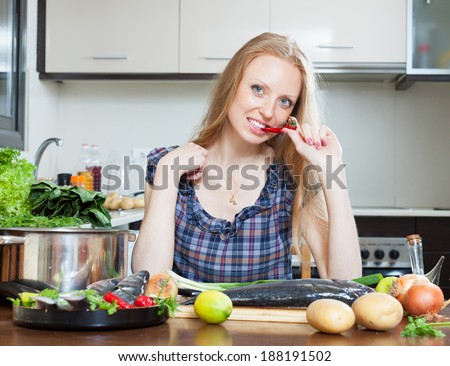 Smiling housewife is thinking how to cook  fish at kitchen