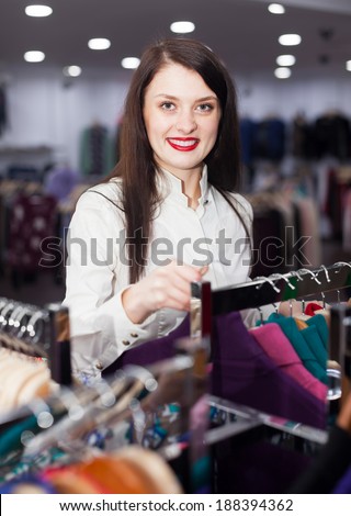 Happy female buyer choosing clothes at fashionable shop
