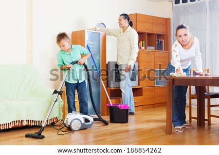 Happy family of three with  boy cleaning with vacuum cleaner in living room