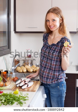 Smiling woman with raw fish and lemon in the kitchen