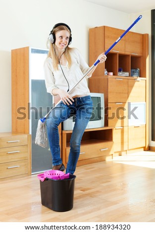 cheerful woman in headphones washing floor with mop