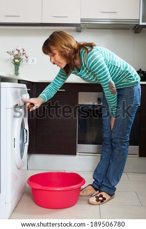 Happy  woman in green doing laundry with washing machine at home
