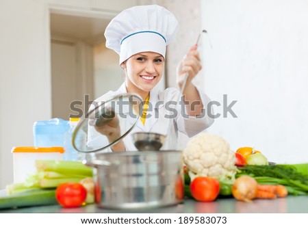 Happy female cook in toque works with ladle