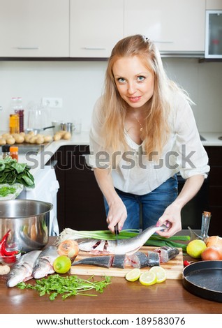 Blonde woman cutting raw fish at kitchen