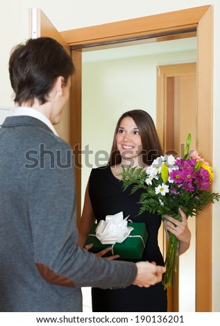 Pretty girl giving flowers and gift to guy at home door