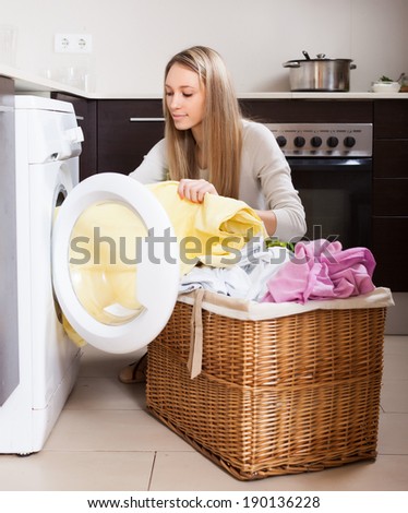 Home laundry. Blonde woman loading clothes into washing machine  in home