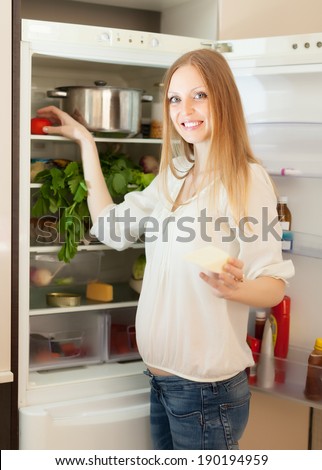 Positive long-haired woman searching for something in refrigerator  at home
