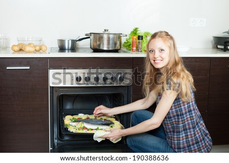 housewife cooking saltwater fish and potatoes on sheet pan in oven