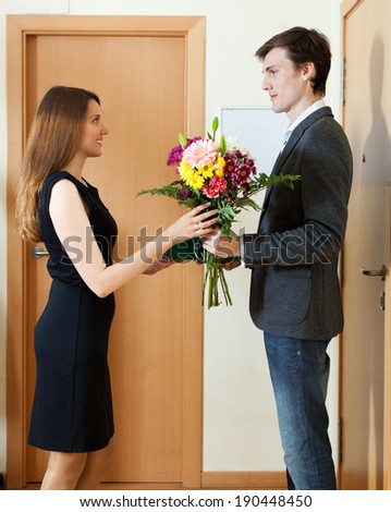 Handsome man giving flowers and gift to woman at home
