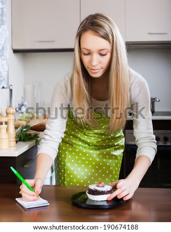 Blonde girl in apron weighing cakes on kitchen scales at table
